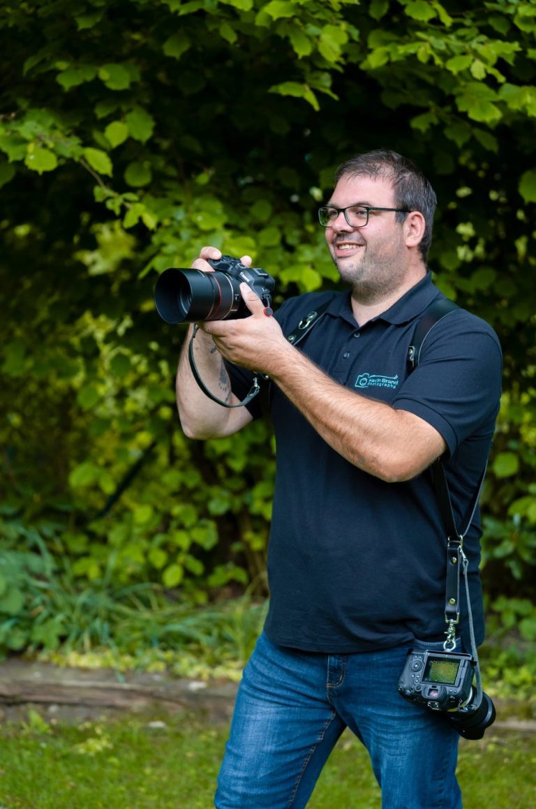 Hochzeitsfotograf aus Bad Driburg Mann mit Kamera liegt grinsend in einem goldenen Feld.