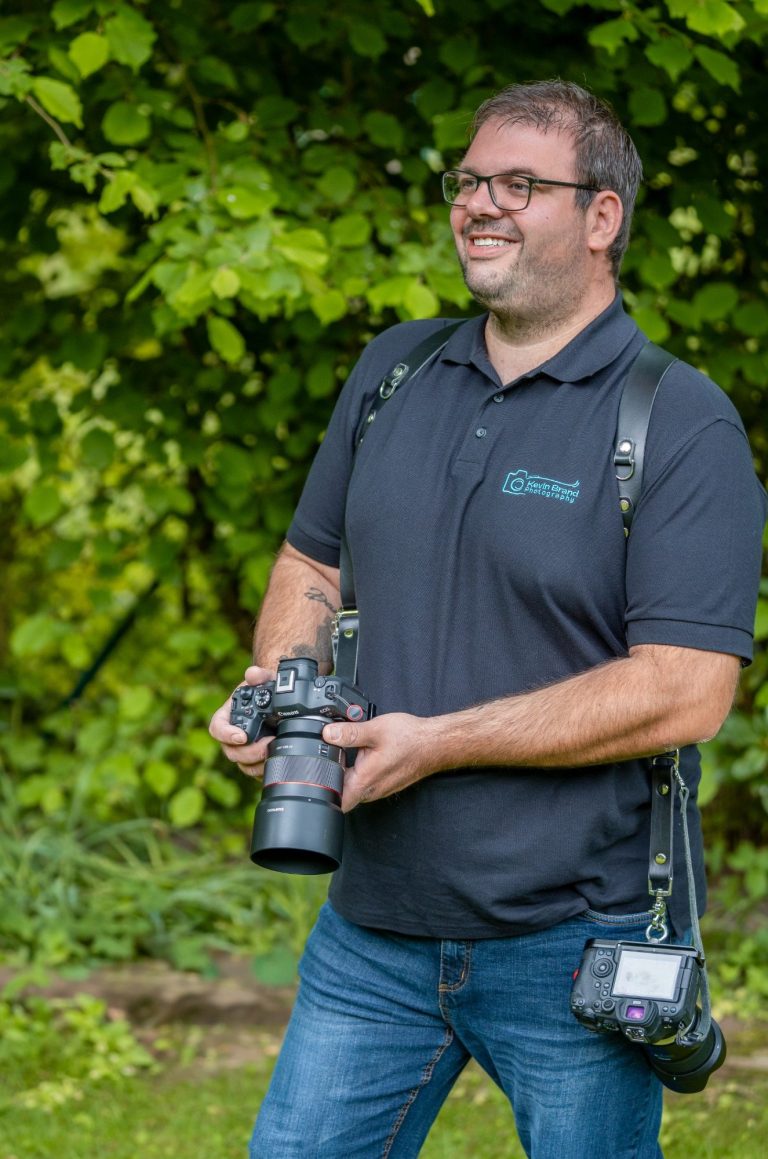 Hochzeitsfotograf aus Bad Driburg Mann mit Kamera liegt grinsend in einem goldenen Feld.